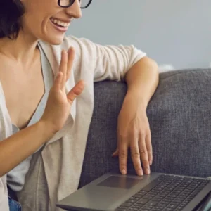 Frau am Laptop, grüßt mit winken ins Laptop, Gesprächpaket