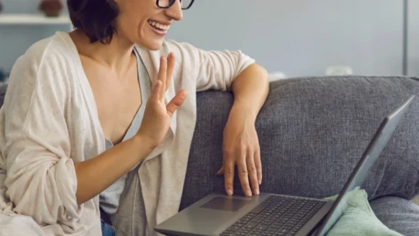 Frau am Laptop, grüßt mit winken ins Laptop, Gesprächpaket